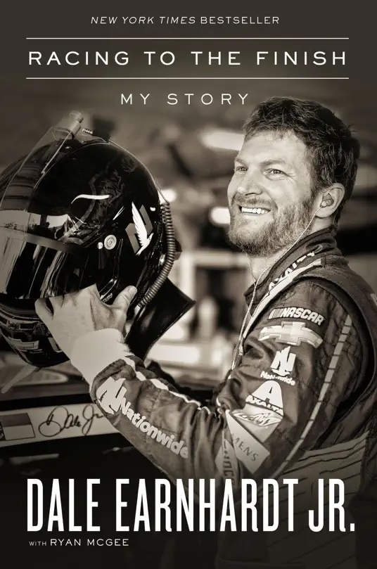 The cover of Racing to the Finish by Dale Earnhardt, Jr. and Ryan McGee, which shows Earnhardt in his race suit smiling and holding his crash helmet